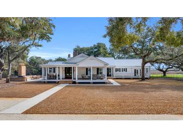 Stunning white farmhouse featuring mature trees, a metal roof, and inviting wrap-around porch at 161 Twelve Oaks Dr., Pawleys Island, SC 29585