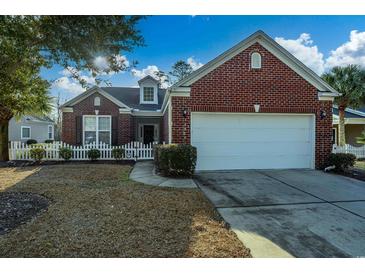 Charming brick home with a well-manicured lawn, white picket fence, and attached two-car garage at 3507 Club Course Dr., North Myrtle Beach, SC 29582