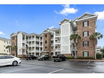 Low angle captures a three story condo with brick accents and covered balconies with black vehicles parked in the lot at 4817 Magnolia Lake Dr. # 104, Myrtle Beach, SC 29577