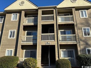 Three-story condo building with multiple balconies, tan siding and neatly manicured landscaping at 300-F Myrtle Greens Dr. # 300-F, Conway, SC 29526