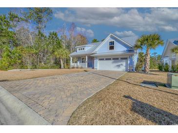 Charming blue home with a metal roof, two-car garage, a brick driveway, and a beautifully landscaped yard with palm trees at 377 Waties Dr., Murrells Inlet, SC 29576