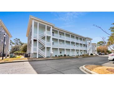 Three-story condo building with pale blue siding, white stairs and railings, and stone accents under a bright blue sky at 4655 Wild Iris Dr. # 101, Myrtle Beach, SC 29577