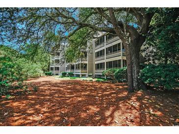 Exterior view of a multi-story building with screened porches surrounded by trees and landscaping at 415 Ocean Creek Dr. # 2202, Myrtle Beach, SC 29572