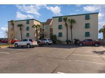 Oceanfront complex with beige stucco and green shutters accented by palm trees and paved parking at 105 S Ocean Blvd. # 108, North Myrtle Beach, SC 29582