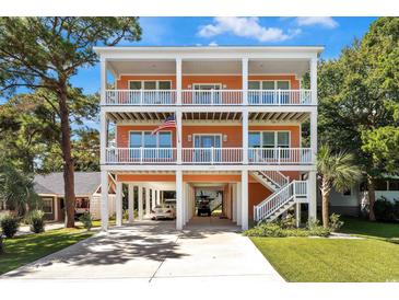 Stunning three-story beach house with white railings, covered parking, and an inviting stairway on a sunny day at 3304 Palm St., North Myrtle Beach, SC 29582