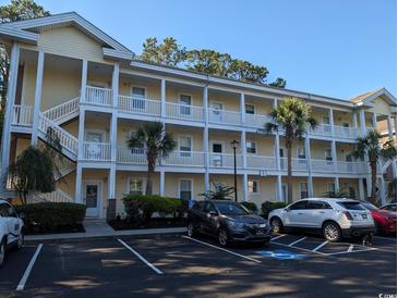 Bright, yellow condo building with multiple balconies, white railings, and palm trees offers a coastal living vibe at 4221 Hibiscus Dr. # 101, Little River, SC 29566