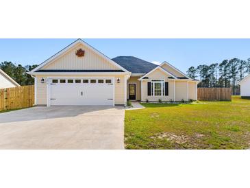 Charming single-story home featuring a two-car garage, manicured lawn and light yellow siding under a blue sky at 5026 Adrian Hwy., Conway, SC 29526