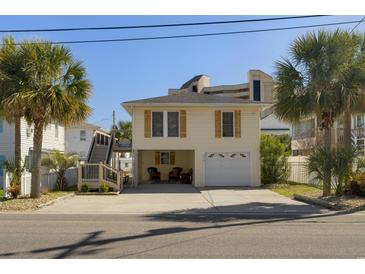 Charming two-story beach home featuring a garage, outdoor seating, and beautiful landscaping with palm trees at 513 Hillside Dr. S, North Myrtle Beach, SC 29582