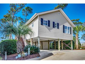Charming raised beach house with light beige siding, dark shutters and a lush, tropical landscaped yard at 9671 Stillwater Ct., Myrtle Beach, SC 29572