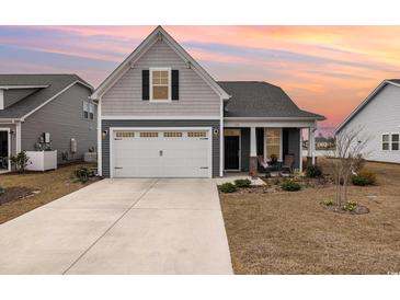Charming home featuring a two-car garage, inviting front porch and manicured lawn set against a picturesque sunset sky at 1881 Moonseed Dr., Longs, SC 29568