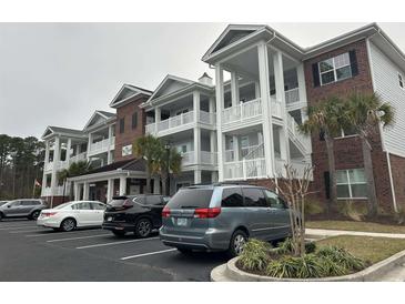 View of condo building with white balconies and brick accents, showcasing covered parking and lush landscaping at 1024 Ray Costin Way # Villa 711, Murrells Inlet, SC 29576
