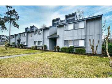 View of the two-story townhome with gray siding, trimmed shrubs and an expansive lawn at 10301 N Kings Hwy. # 15-8, Myrtle Beach, SC 29572