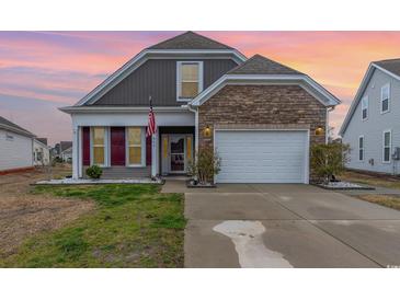 Charming two-story home featuring a stone accent wall, two car garage, and an American flag at 909 Witherbee Way, Little River, SC 29566