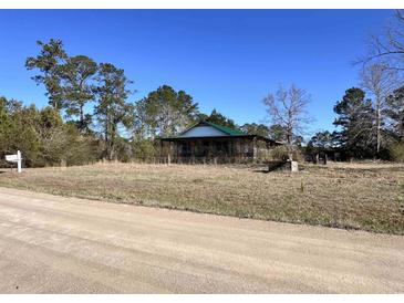 Exterior view of a home with a green metal roof and a covered porch, surrounded by trees and a dirt road at 1264 Harrelson Dr., Longs, SC 29568