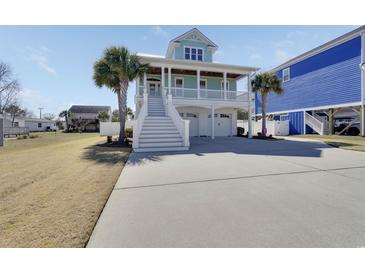 Charming two-story home featuring a covered porch, white railings, palm trees, and a spacious driveway at 417 Seabreeze Dr., Garden City Beach, SC 29576