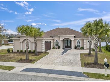 Stucco home featuring an arched double-door entryway, brick drive, meticulous landscaping, and palm trees at 1012 Dowitcher Dr., Conway, SC 29526