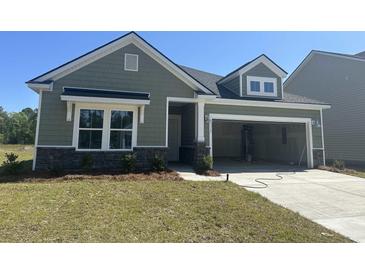 Charming single-Gathering home featuring green siding, stone accents, and an attached two-car garage at 3317 Sw Wood Stork Dr., Ocean Isle Beach, NC 28469