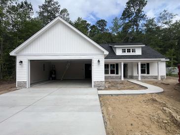 New construction single-story home with white siding, stone accents, open garage, and a concrete driveway and sidewalk at 1274 Pinetucky Dr., Galivants Ferry, SC 29544