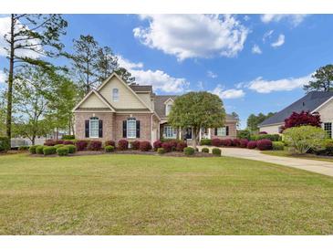Beautiful brick home featuring mature landscaping, a sprawling green lawn, and elegant black shutters at 9278 Nw Checkerberry Square, Calabash, NC 28467