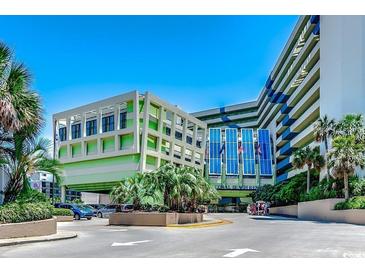 View of the exterior of the Coral Beach Resort, featuring a light green facade and tropical landscaping at 1105 S Ocean Blvd. # 502, Myrtle Beach, SC 29577