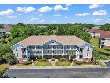 Aerial view of a condo building featuring a well-manicured lawn and ample parking surrounded by lush trees under a blue sky at 5750 Oyster Catcher Dr. # 1135, North Myrtle Beach, SC 29582