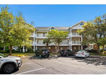 Exterior view of a three-story condo building with white balconies, lush landscaping, and ample parking at 6015 Catalina Dr. # 132, North Myrtle Beach, SC 29582