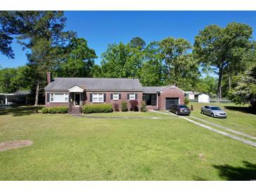Charming brick home with manicured lawn, attached garage, and long driveway, surrounded by mature trees under a clear blue sky at 408 South Farr Ave., Andrews, SC 29510