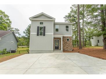 Two-story home with gray siding, stone accents, and a large concrete driveway surrounded by natural landscaping at 2212 Dykman Circle, Little River, SC 29566