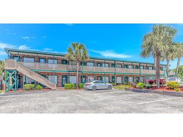 Two-story condo building with brick exterior, green trim, palm trees, and parking lot under a bright blue sky at 4516 Seaview St. # 135, North Myrtle Beach, SC 29582