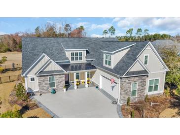 Two-story home featuring a stone and grey siding exterior, black roof, and a spacious driveway with yellow chairs on the front porch at 1004 Whooping Crane Dr., Conway, SC 29526