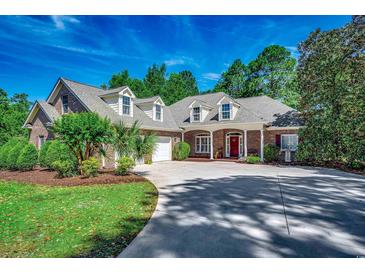 Charming brick home featuring a red door, dormer windows, lush landscaping and a curving driveway at 4363 Parkland Dr., Myrtle Beach, SC 29579