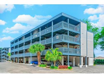 Multi-level condo building boasts ample parking, palm trees, and blue accents against a clear blue sky at 1500 Cenith Dr. # D 103, North Myrtle Beach, SC 29582