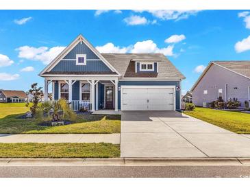 Charming blue home with a two-car garage, landscaped yard, and inviting front porch on a sunny day at 684 Wailea Circle, Little River, SC 29566