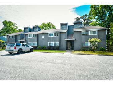 View of building exterior with gray wood siding, windows, roof access, landscaping, and asphalt parking lot at 10301 N Kings Hwy. # 21-5, Myrtle Beach, SC 29572