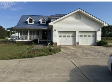 Charming white two-story home with a blue metal roof, front porch, and a two car garage at 3293 Schoolhouse Dr., Hemingway, SC 29554