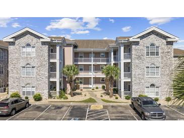 Three-story condo building featuring stone accents, white railings, balconies, and palm trees in a paved parking area at 4737 Wild Iris Dr. # 203, Myrtle Beach, SC 29577