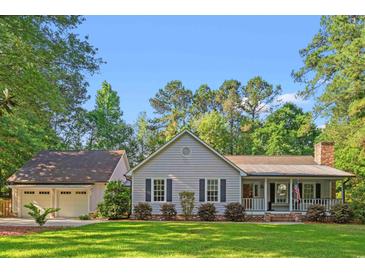 Charming single-story home with a well-manicured lawn and a detached two-car garage, set amongst mature trees at 57 River Birch Ln., Pawleys Island, SC 29585