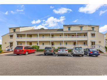 Multi-level condo building with yellow exterior and multiple cars parked in front on a sunny day at 1100 Possum Trot Rd. # D-205, North Myrtle Beach, SC 29582