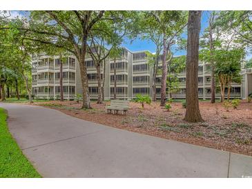 View of the condo complex surrounded by trees, landscaping, and a walking path with a bench at 415 Ocean Creek Dr. # 2245, Myrtle Beach, SC 29572