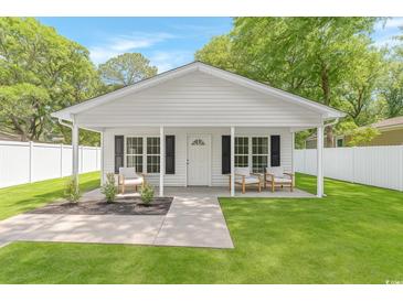 Charming home featuring a covered porch, inviting chairs, and lush green lawn at 23 Gabe Pl., Pawleys Island, SC 29585