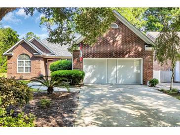 Brick home featuring a two-car garage and a well-manicured front yard with mature trees and plantings at 3071 Alice Ln., Little River, SC 29566