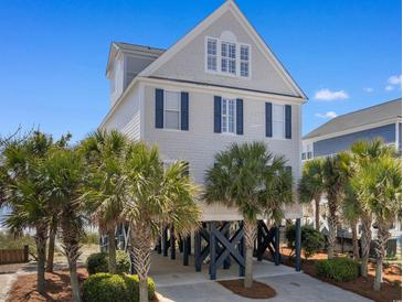 Charming stilted home with palm trees offers coastal living at its finest with dark blue shutters and beach views at 703 S Waccamaw Dr., Garden City Beach, SC 29576