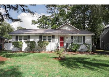 Charming single-story home featuring a metal roof, white painted brick, well-manicured landscaping, and a vibrant red front door at 1014 Bay Dr., Surfside Beach, SC 29575