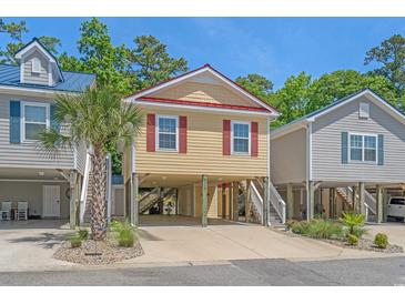 Charming raised beach house with yellow siding, red shutters, and a red roof situated between two other beach houses at 4319 Grande Harbour Blvd., Little River, SC 29566