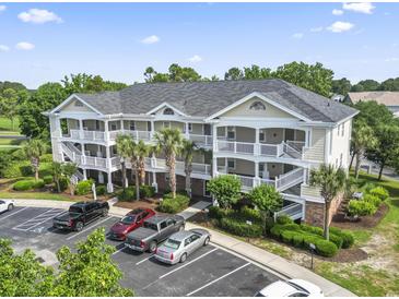 A three-story condo building with white railings, palm trees, and a parking lot in a sunny setting at 5801 Oyster Catcher Dr. # 332, North Myrtle Beach, SC 29582