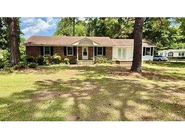 Charming brick home featuring a well-maintained lawn, complemented by mature trees and classic black shutters at 6805 Mclaurin Rd., Mullins, SC 29574