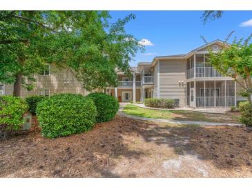 Exterior view of a two-story building with tan siding, white trim, and multiple balconies, nestled among mature trees at 3104 Sweetwater Blvd. # 3104, Murrells Inlet, SC 29576