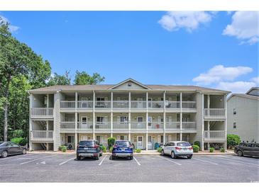Three-story condo building with multiple balconies, parking spaces, and lush landscaping on a sunny day at 1460 Blue Tree Ct. # E, Myrtle Beach, SC 29588