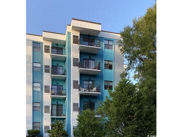 Modern condo building featuring private balconies with black metal railings, teal and white paint scheme, and lovely landscaping at 5001 Little River Rd. # W-211, Myrtle Beach, SC 29577