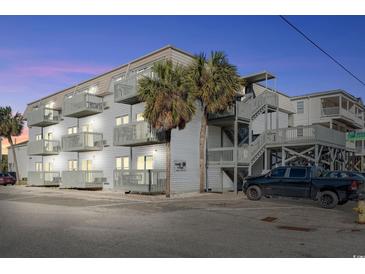 Three-story condominium building featuring stairwells and multiple balconies, surrounded by trees and ample parking spaces at 300 47Th Ave. S # 1F, North Myrtle Beach, SC 29582